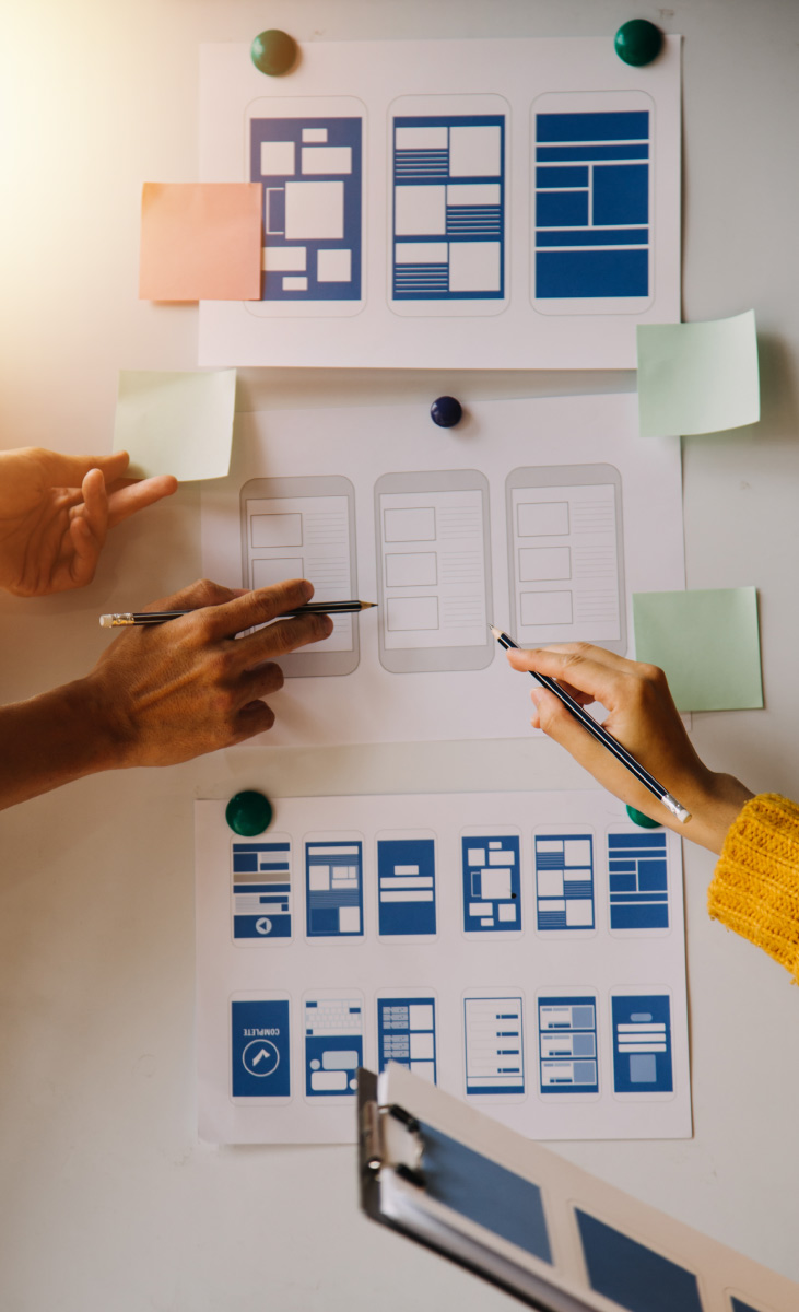 Manos de un equipo organizando bocetos (wireframes) de una aplicación móvil en un tablero, durante la fase de prototipado de un curso de Design Sprint.